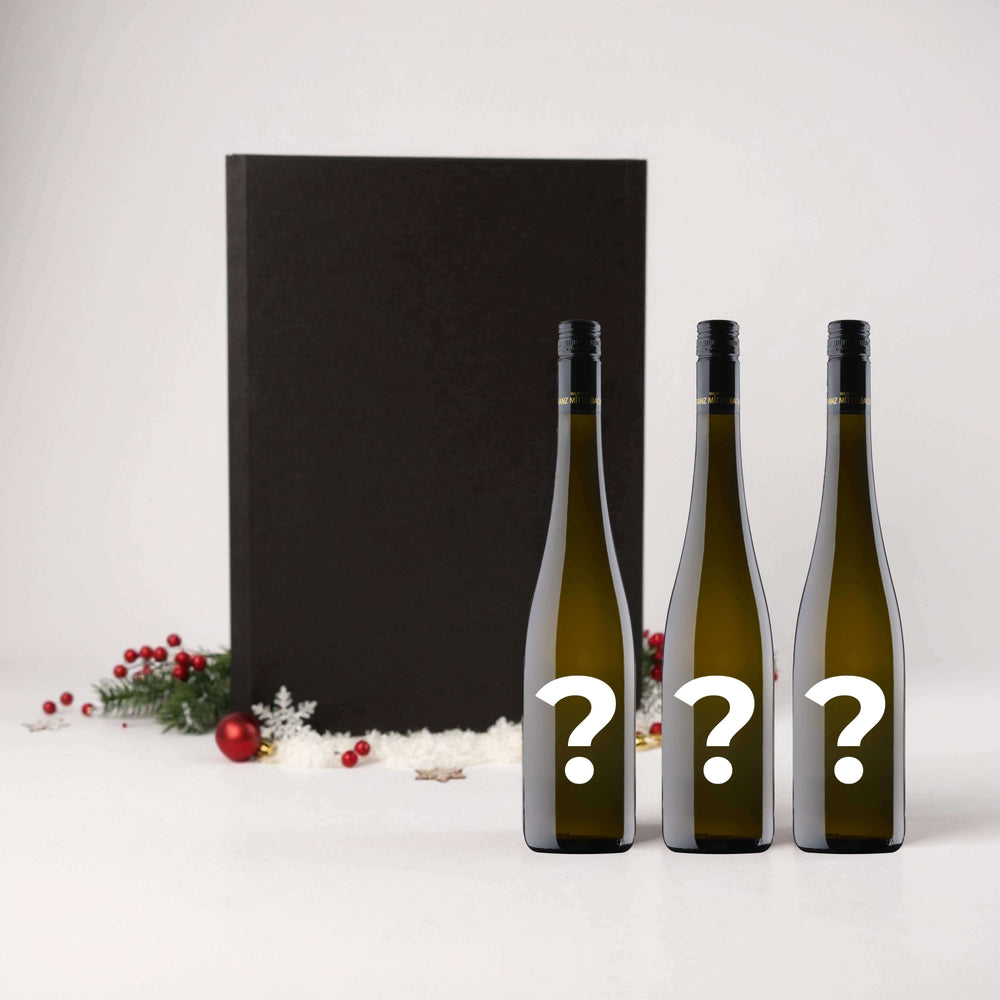 Individuelles 3er Weihnachtspaket mit drei geheimen Weinflaschen vor festlicher Kulisse.