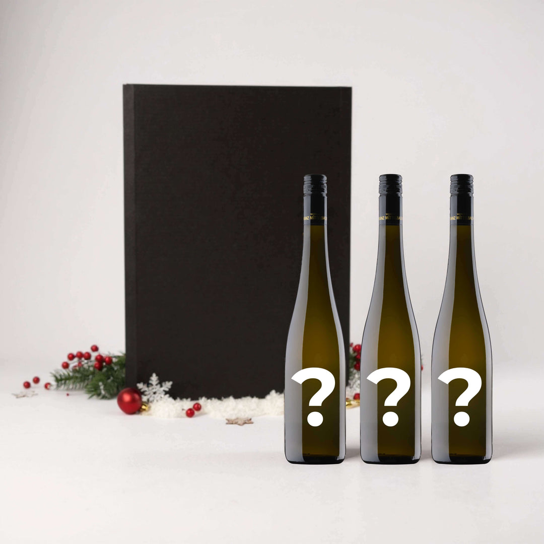 Individuelles 3er Weihnachtspaket mit drei geheimen Weinflaschen vor festlicher Kulisse.